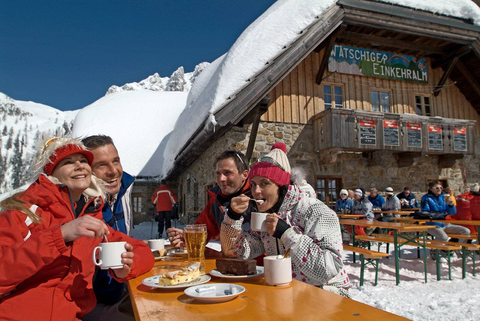 Skiers with coffee and cake on a sunny mountain hut terrace