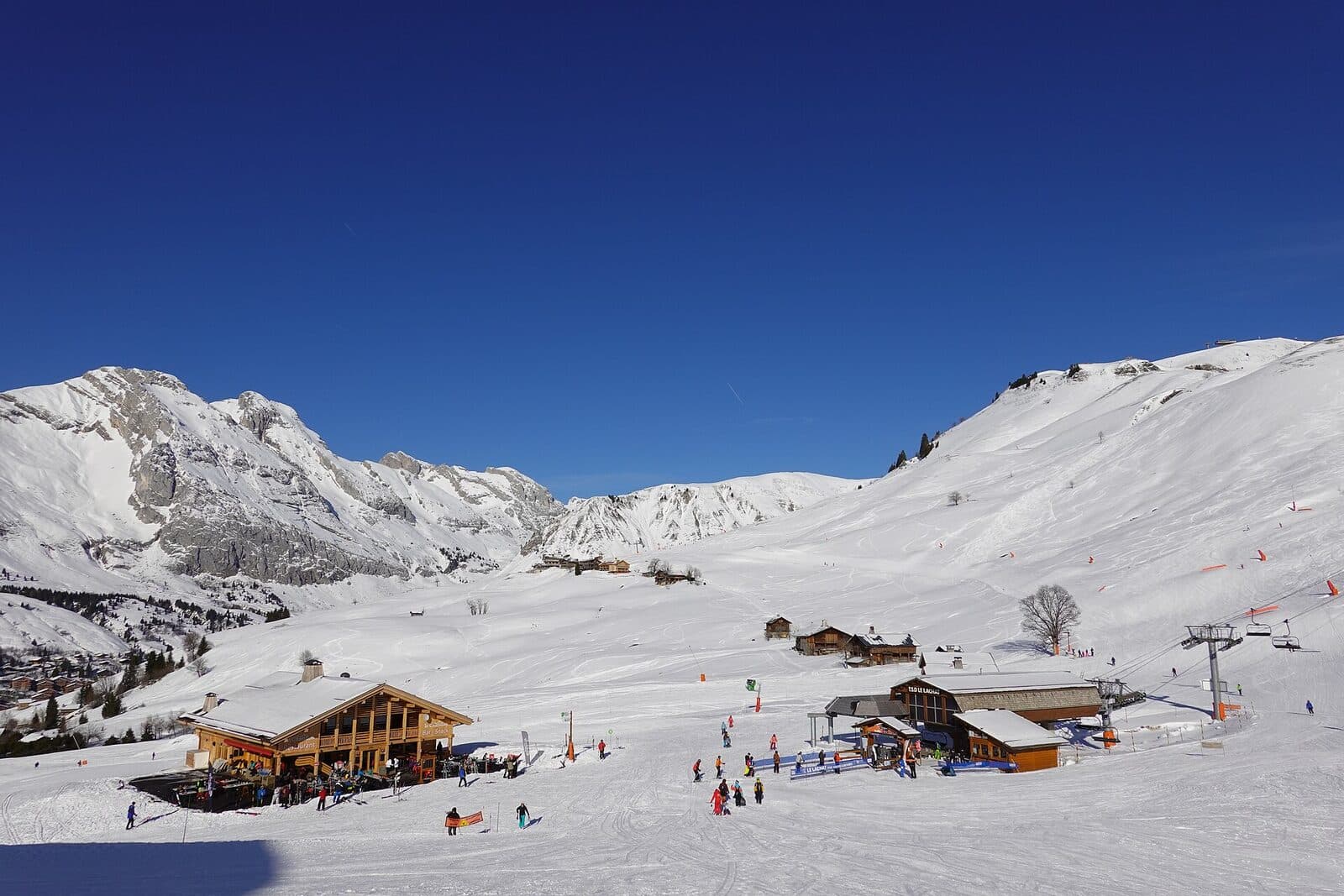 The beginner area at La Côte above Le Grand-Bornand, with a chalet restaurant, a chairlift and skiers in the sun