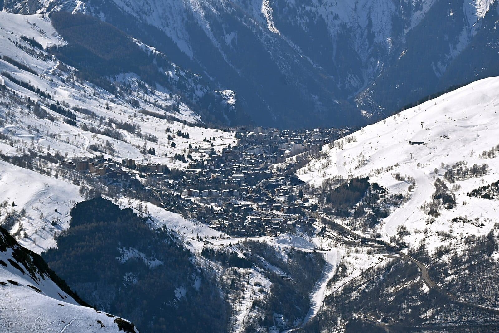 Les Deux Alpes spread across its snowy plateau, seen from across the valley, with pistes on the slopes either side