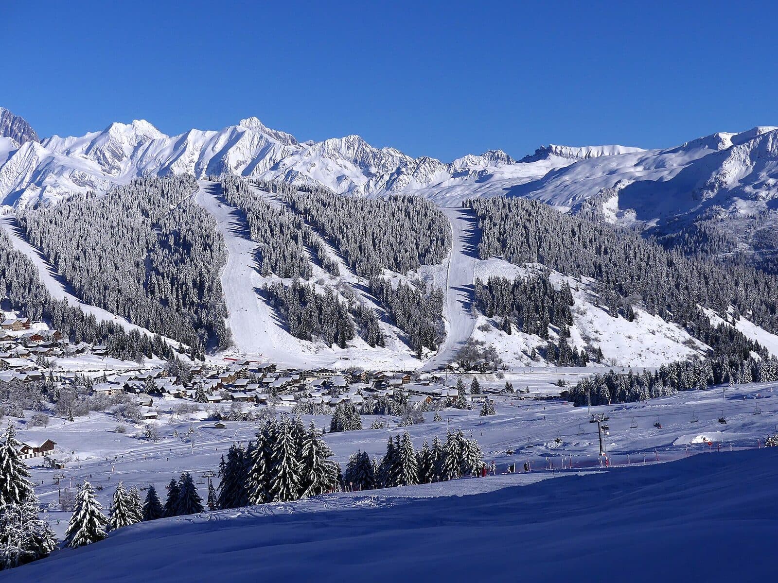Les Saisies spread below its forested ski slopes on a bright winter day, with snowy peaks behind