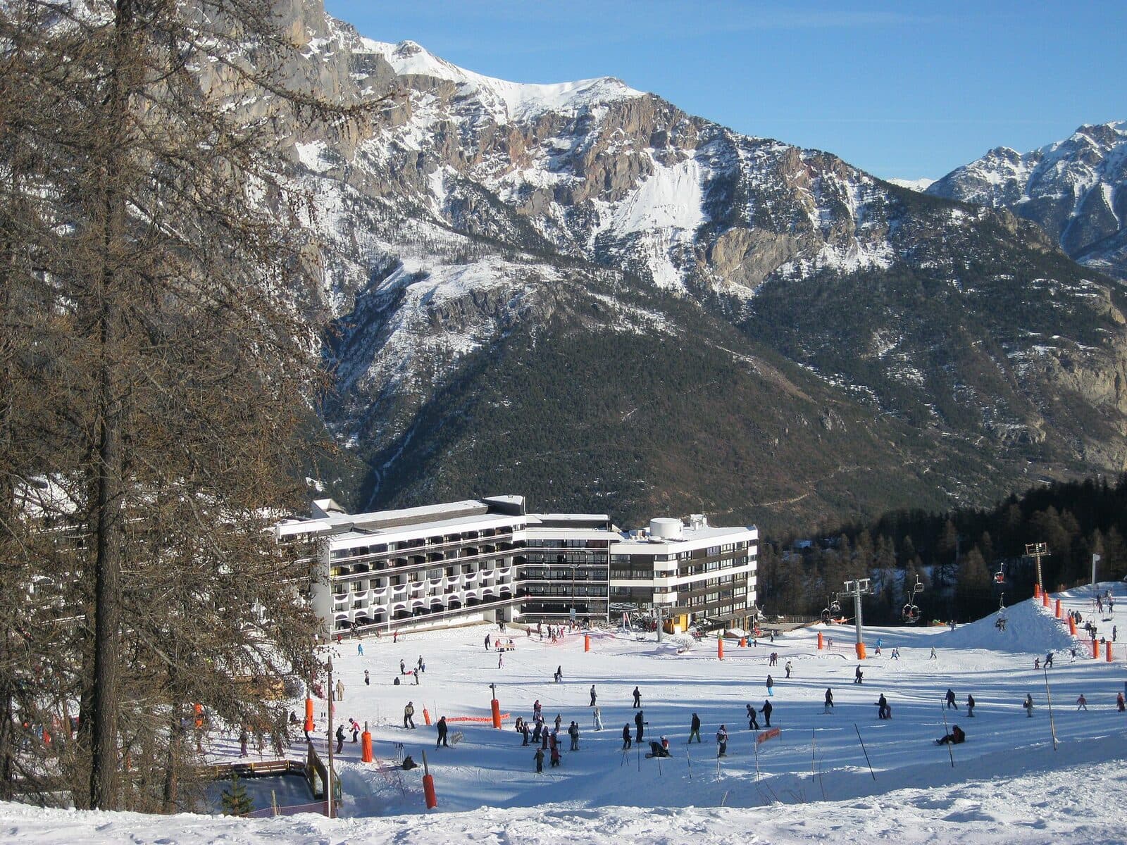Skiers on the busy beginner area at the foot of Puy-Saint-Vincent 1600, below rocky snow-dusted peaks