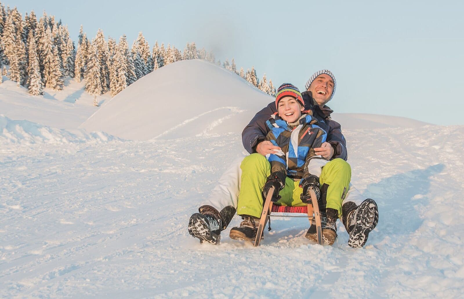 A laughing father and son racing downhill on a wooden sledge