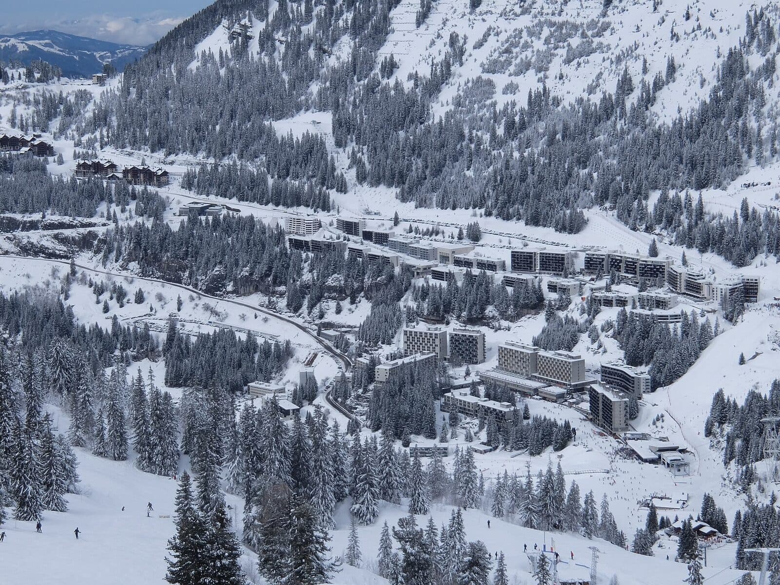 The modernist apartment blocks of Flaine among snowy firs, with skiers on the pistes below