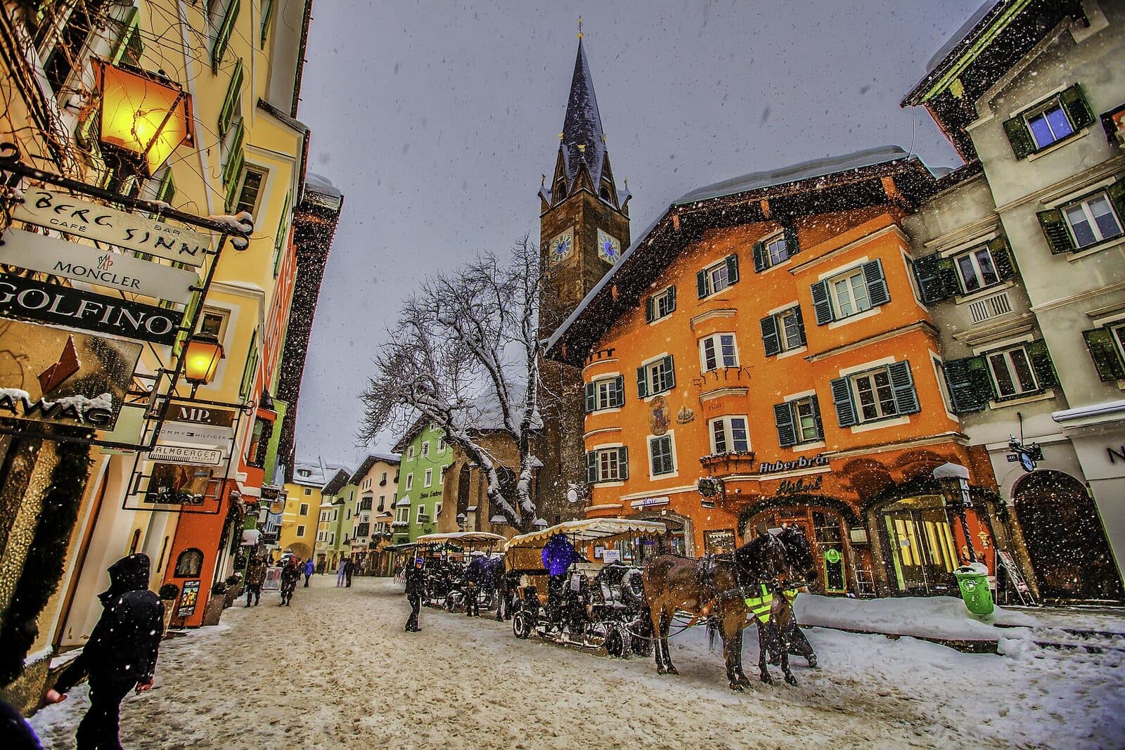 Horse-drawn carriages wait in Kitzbühel's snowy old town, below a church tower